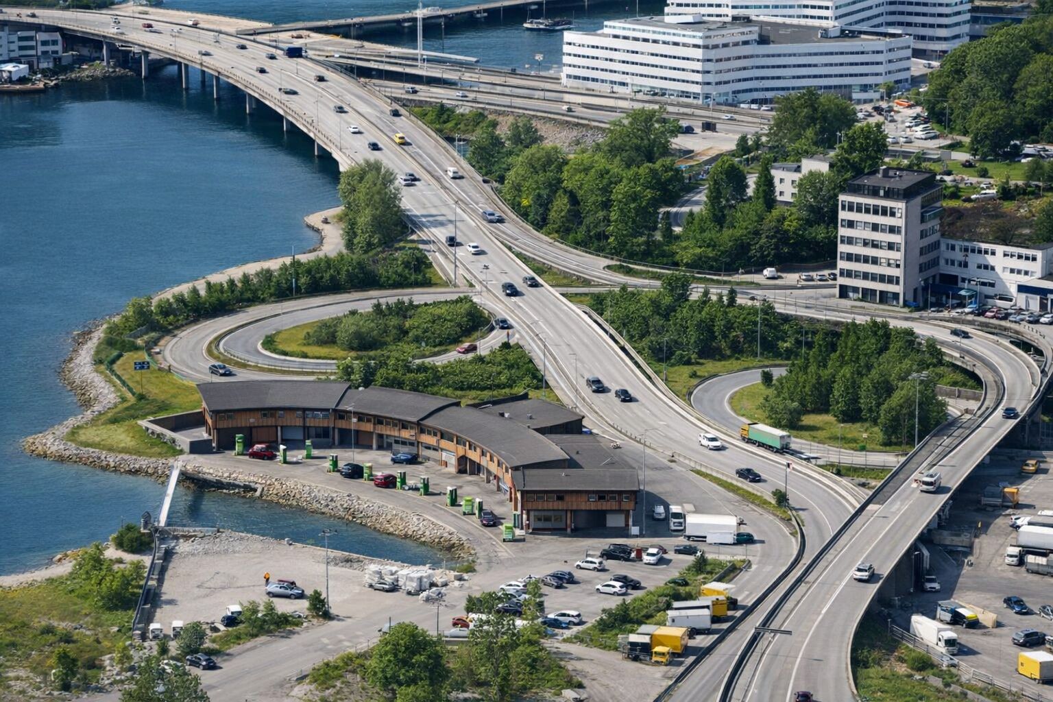 Ilmakuva monitasoisesta moottoritieliittymästä ja latausasemasta meren rannalla.